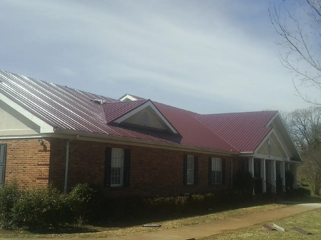 Red metal roof with gabled entries on a long brick building, from a Hail Damage Roof Repair job in Shirley