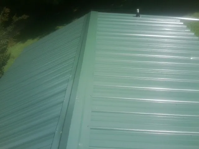 New green metal panels meeting at the ridge of a roof — Flat Roof Repair work by our crew in Shirley