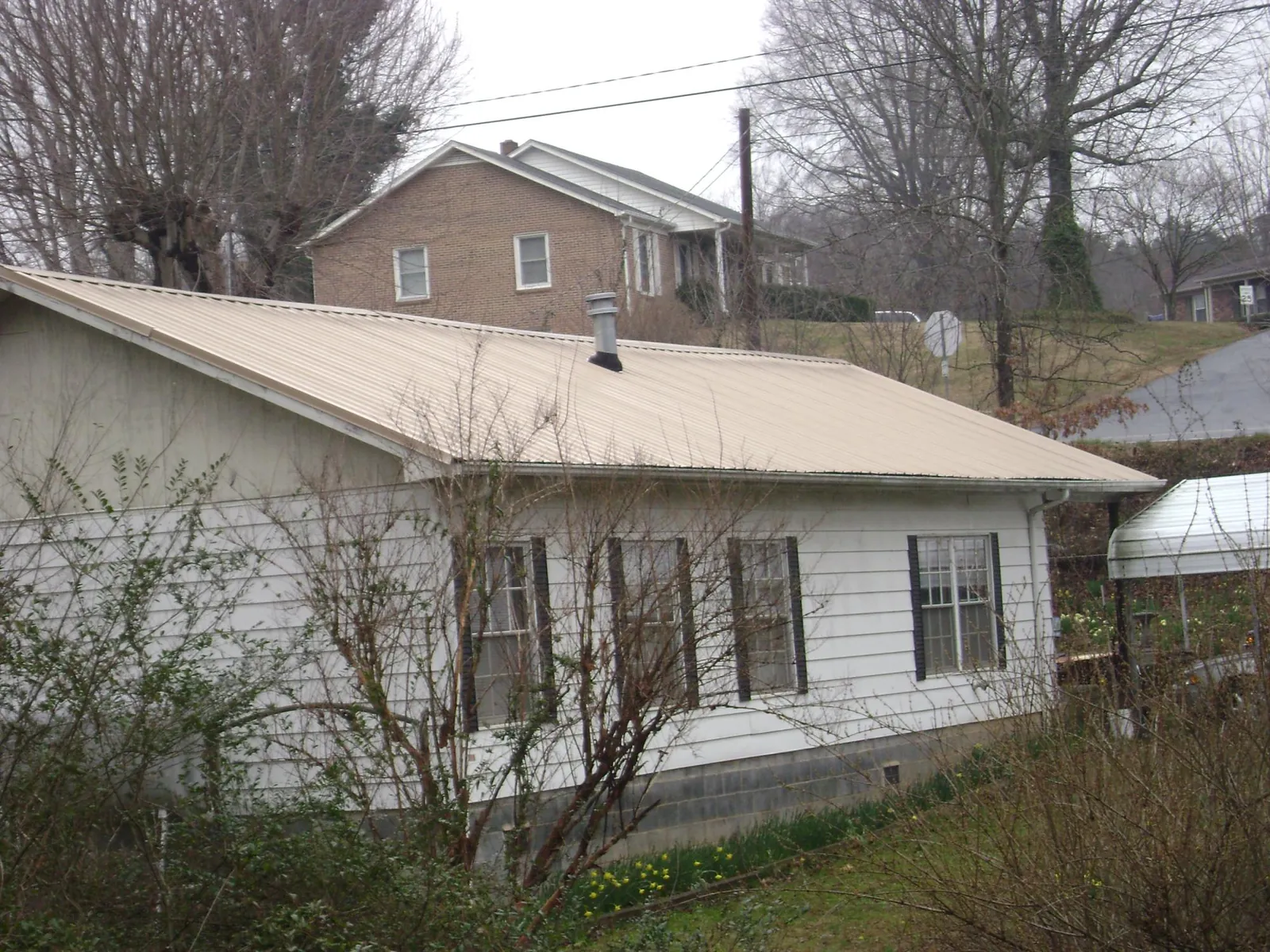 Tan metal roof on a white sided house set into a hillside — Commercial Roofing by Roofing Brothers in Shirley